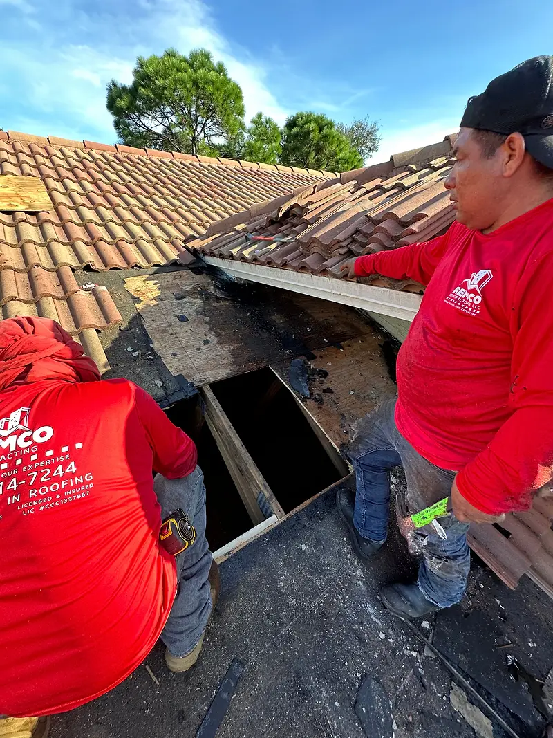 Two Remco roofers repairing decking under a tile roof